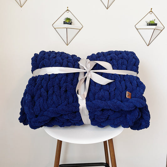 Blue knitted blanket with a white ribbon on a white chair against a light background