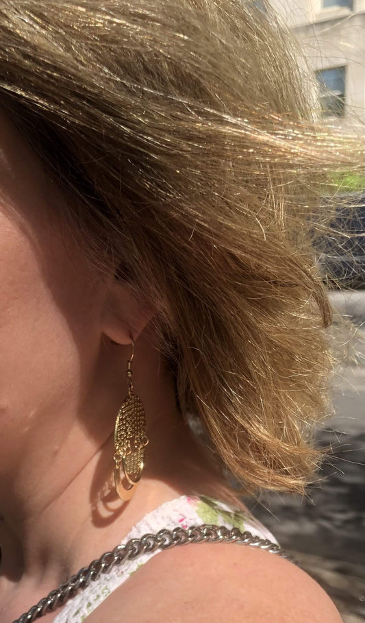 Close-up of a person wearing gold earrings with a blurred background
