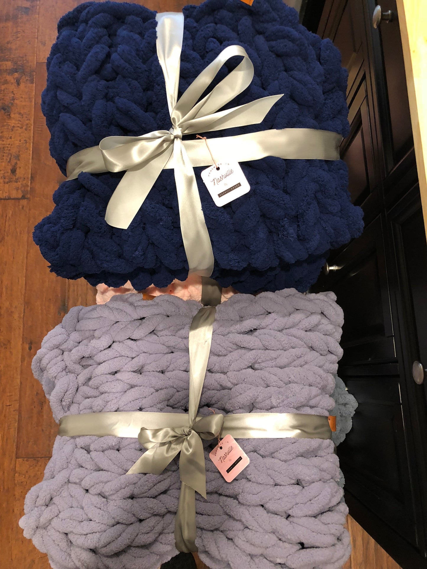 Two knitted blankets, one blue and one gray, with ribbons and tags on a wooden surface.
