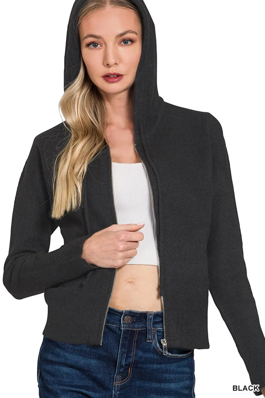Woman wearing a black hooded jacket over a white top and blue jeans on a white background