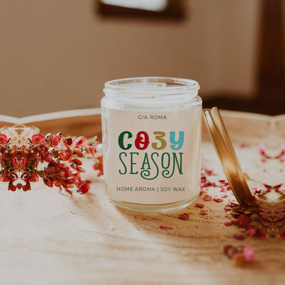 Cozy Season Candle with metal top leaning against candle on table