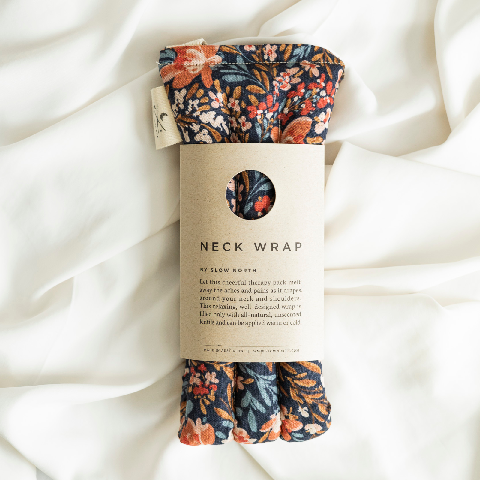 Neck wrap with floral pattern on packaging against a white fabric background