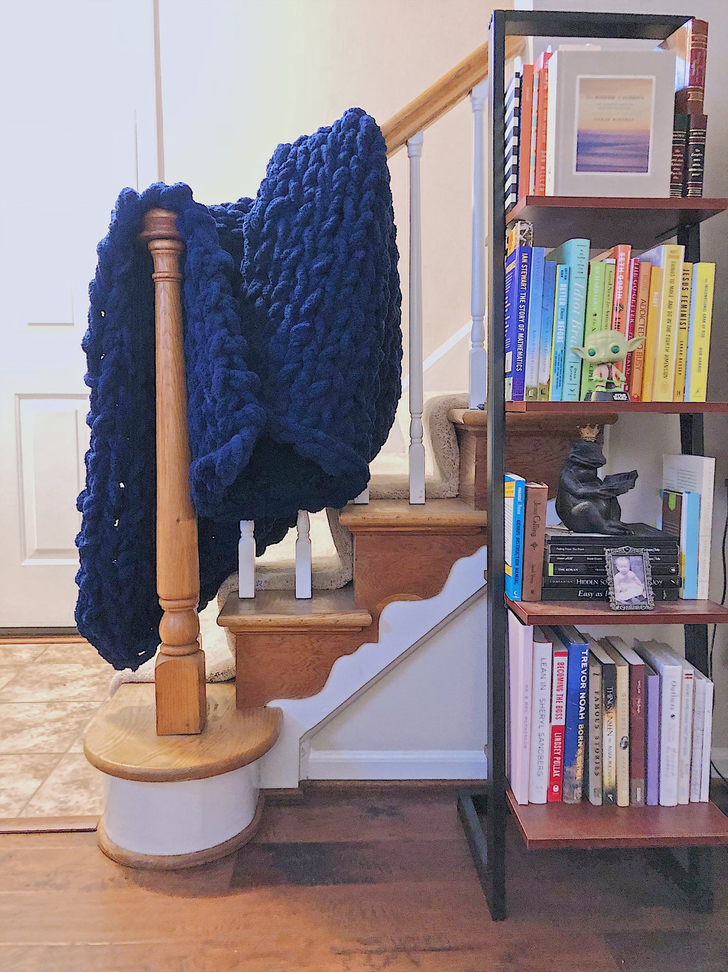 Navy blue knitted blanket draped over a wooden staircase with a bookshelf filled with books in the background.