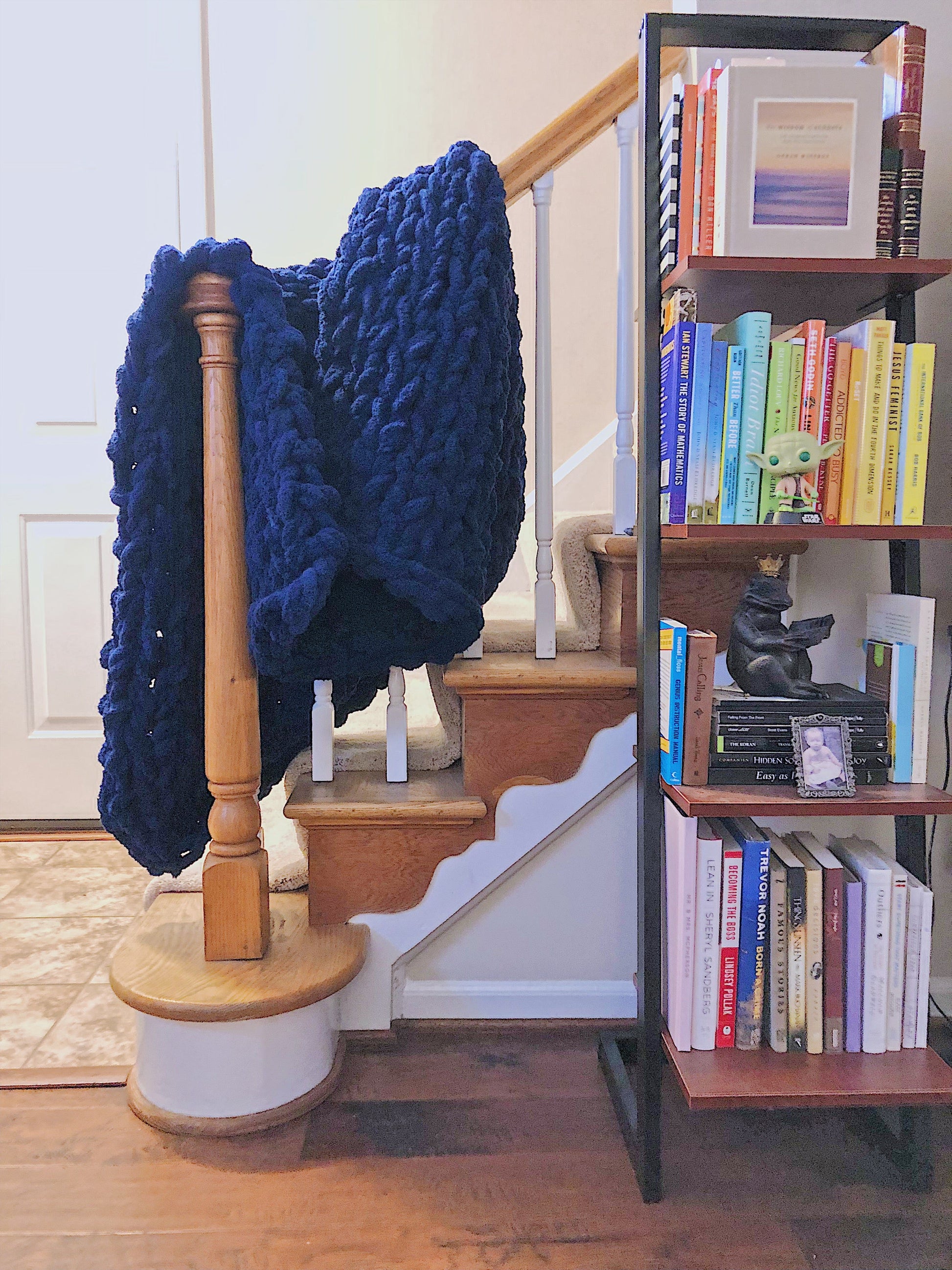 Navy blue knitted blanket draped over a wooden staircase with a bookshelf filled with books in the background.