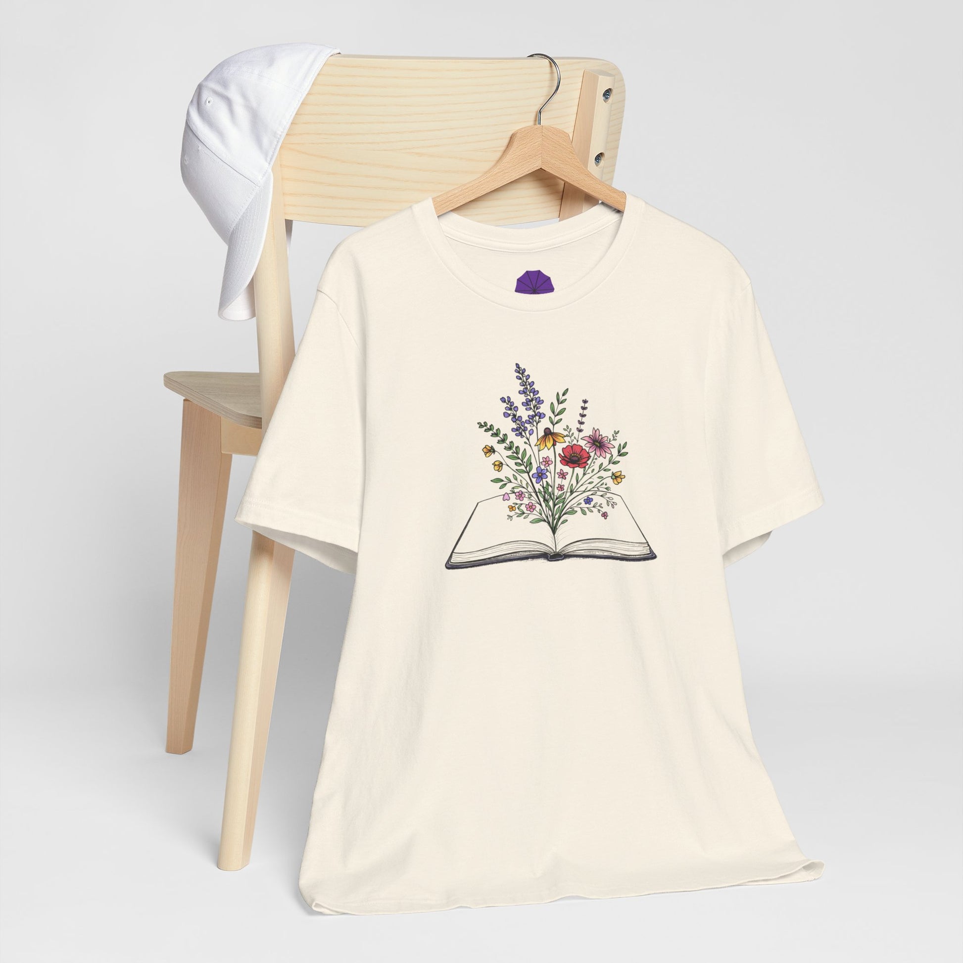 Beige t-shirt with floral book design on a wooden chair against a white background