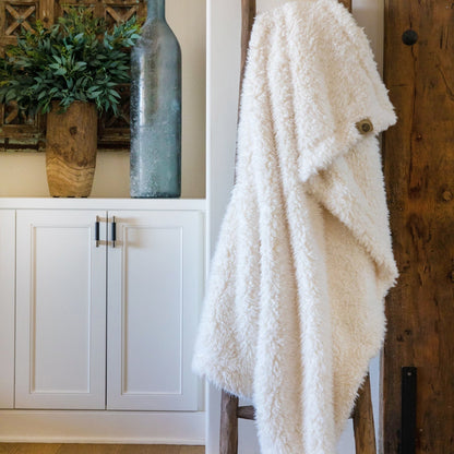 White textured blanket draped over a wooden chair in a room with white cabinets and decorative elements.