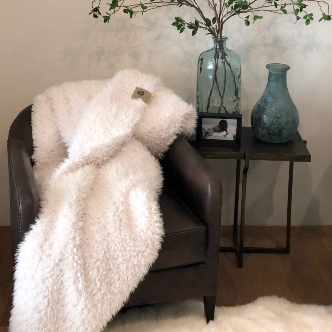 White fluffy blanket draped over a brown armchair with a side table featuring decorative items.