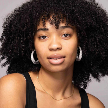 Woman with curly hair wearing white Dove bamboo Lucite hoop earrings