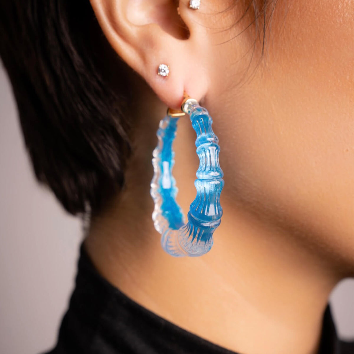 Side view of a woman wearing bright blue Fiji bamboo Lucite hoop earrings
