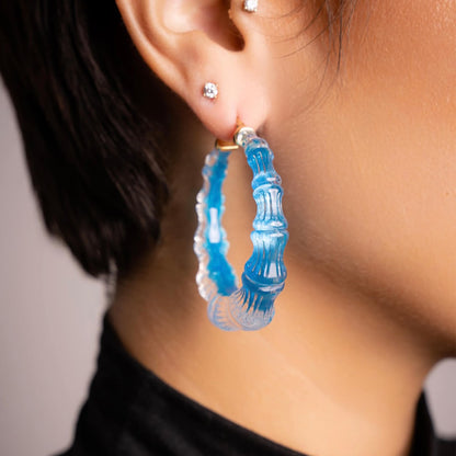 Side view of a woman wearing bright blue Fiji bamboo Lucite hoop earrings
