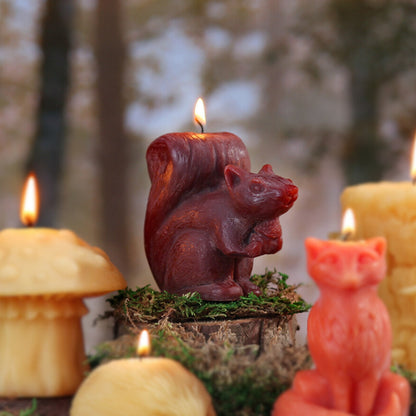 Red beeswax squirrel candle on a mossy log with lit beeswax candles in the woods