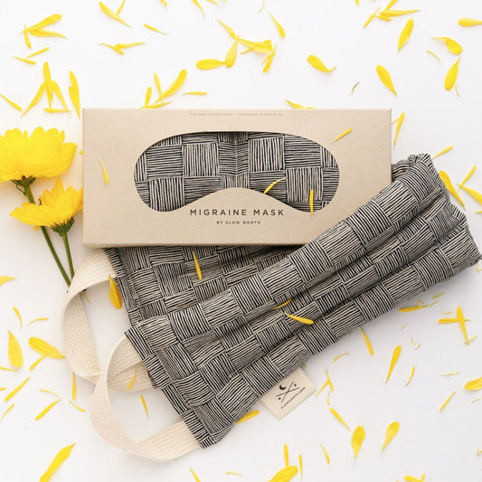 Haystack eye mask in its gift box beside the matching neck wrap, styled with yellow flowers