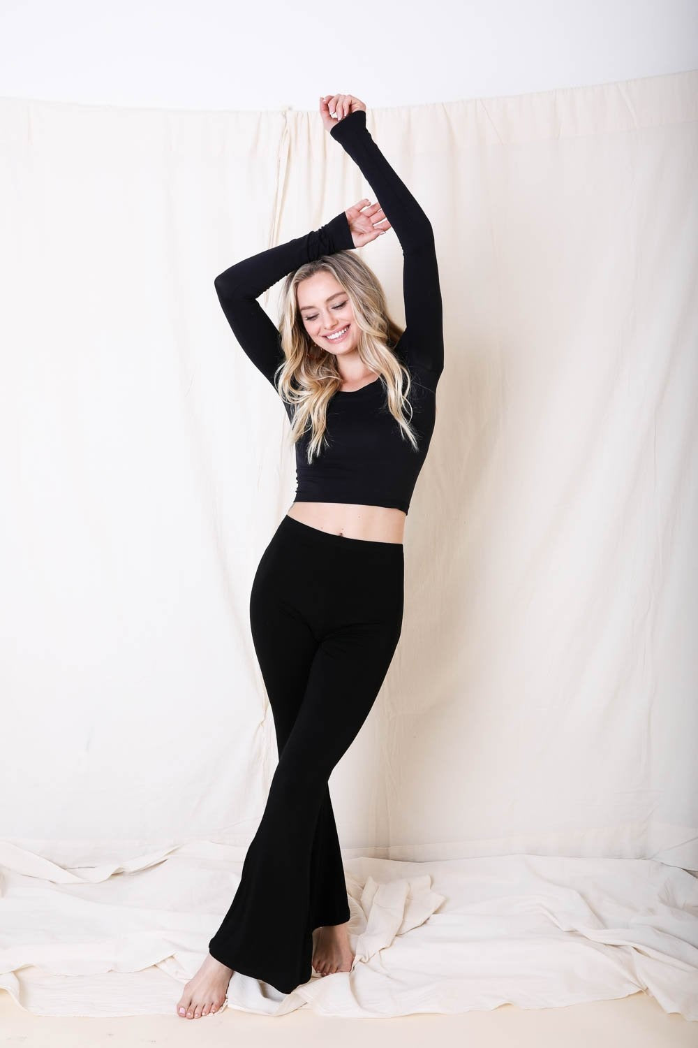 Woman in black outfit posing against a white curtain
