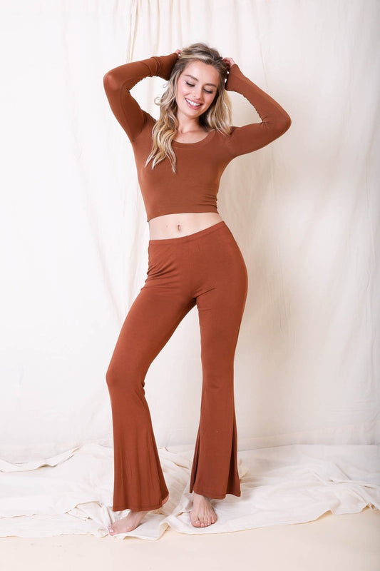 Woman wearing a brown long-sleeve top and flared pants against a white background
