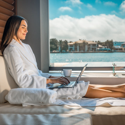 Woman on laptop in Luxury Organic Bathrobe in Bed by Window it is a beautiful day outside and she is on a laptop - ShopPurpleUmbrella