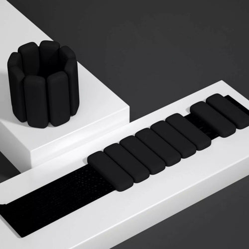 Black silicone wrist and ankle weight bangles with adjustable Velcro strap on white styled surface