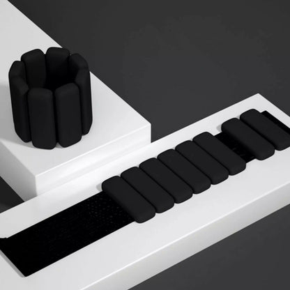 Black silicone wrist and ankle weight bangles with adjustable Velcro strap on white styled surface