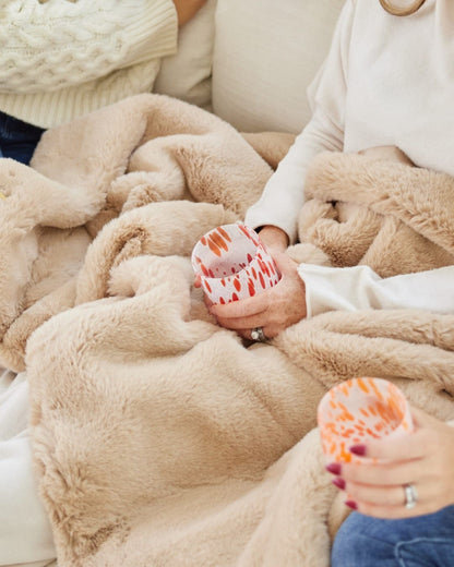 Hands holding a patterned mug over the plush faux fur lap blanket in Camel