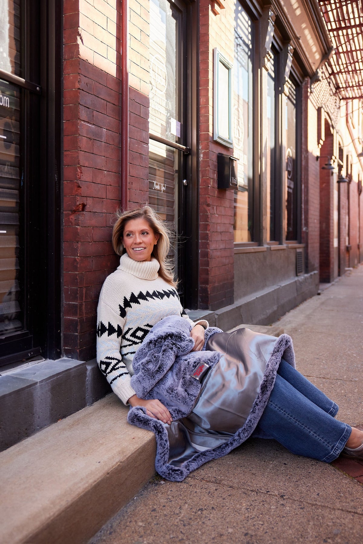 Woman sitting on brick front steps with the faux fur lap blanket in Silver over her knees