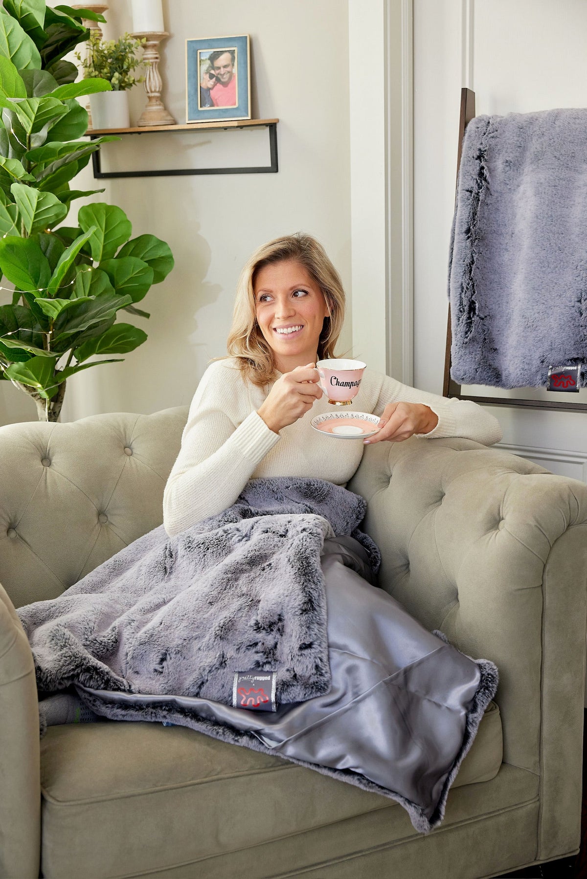 Woman relaxing on a sofa under the Pretty Rugged faux fur lap blanket in Silver