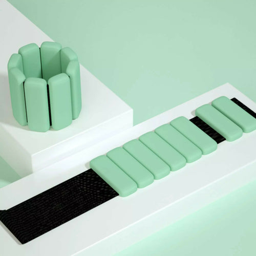 Green silicone wrist and ankle weight bangles with adjustable Velcro strap on white styled surface