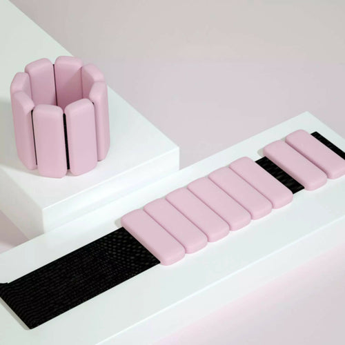 Pink silicone wrist and ankle weight bangles with adjustable Velcro strap on white styled surface
