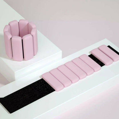 Pink silicone wrist and ankle weight bangles with adjustable Velcro strap on white styled surface